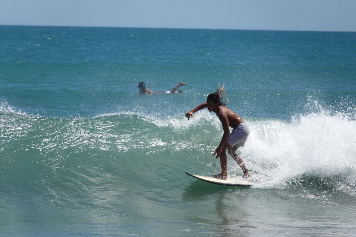 Kalong riding a wave on a white surfboard